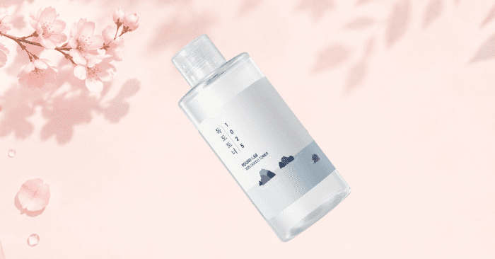 Korean skincare essence bottle on a soft pink background with cherry blossoms representing hydration and glowing glass skin aesthetic
